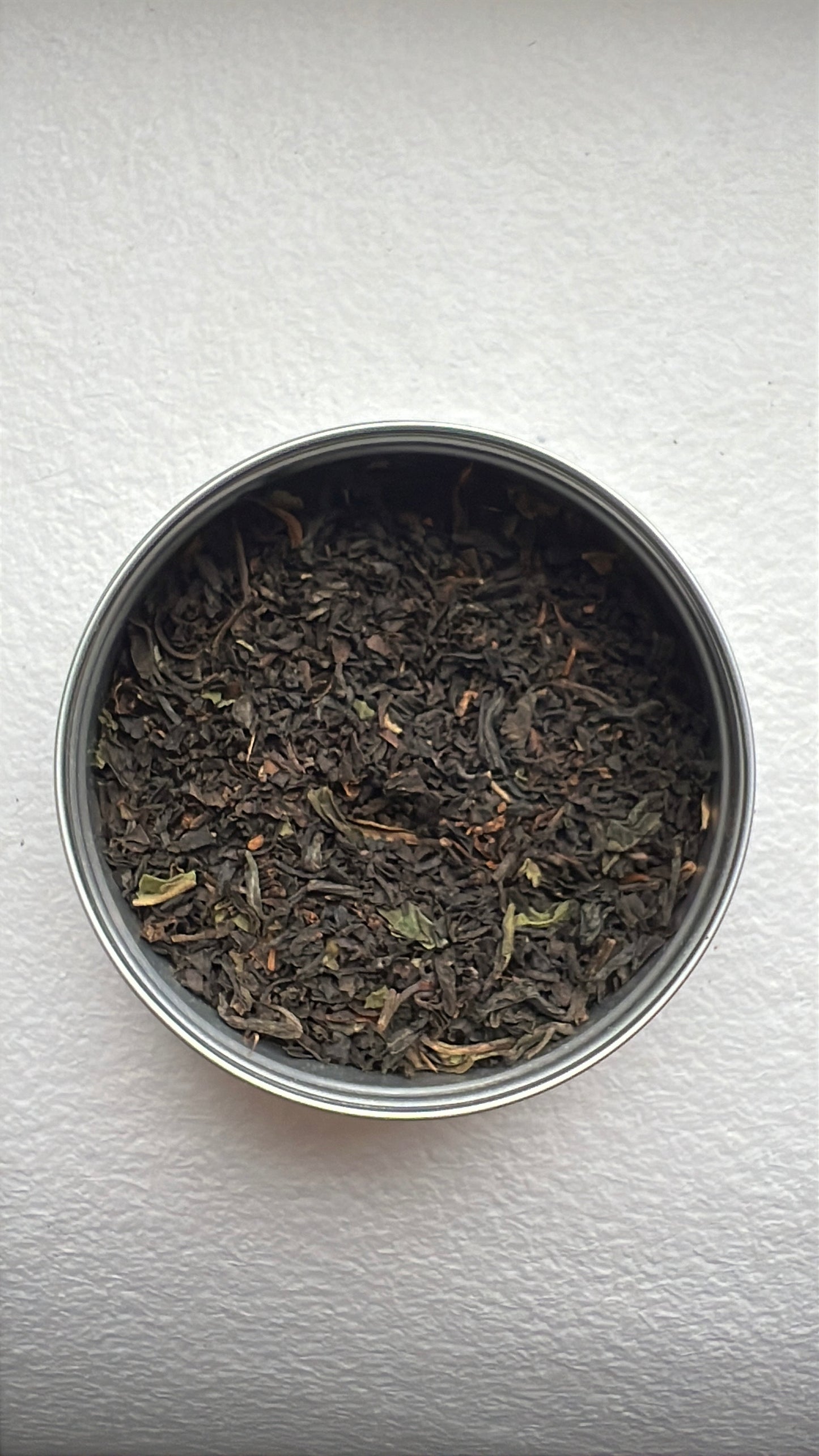 Metal canister filled with black organic tea leaves on a white background by Mull Tea Company