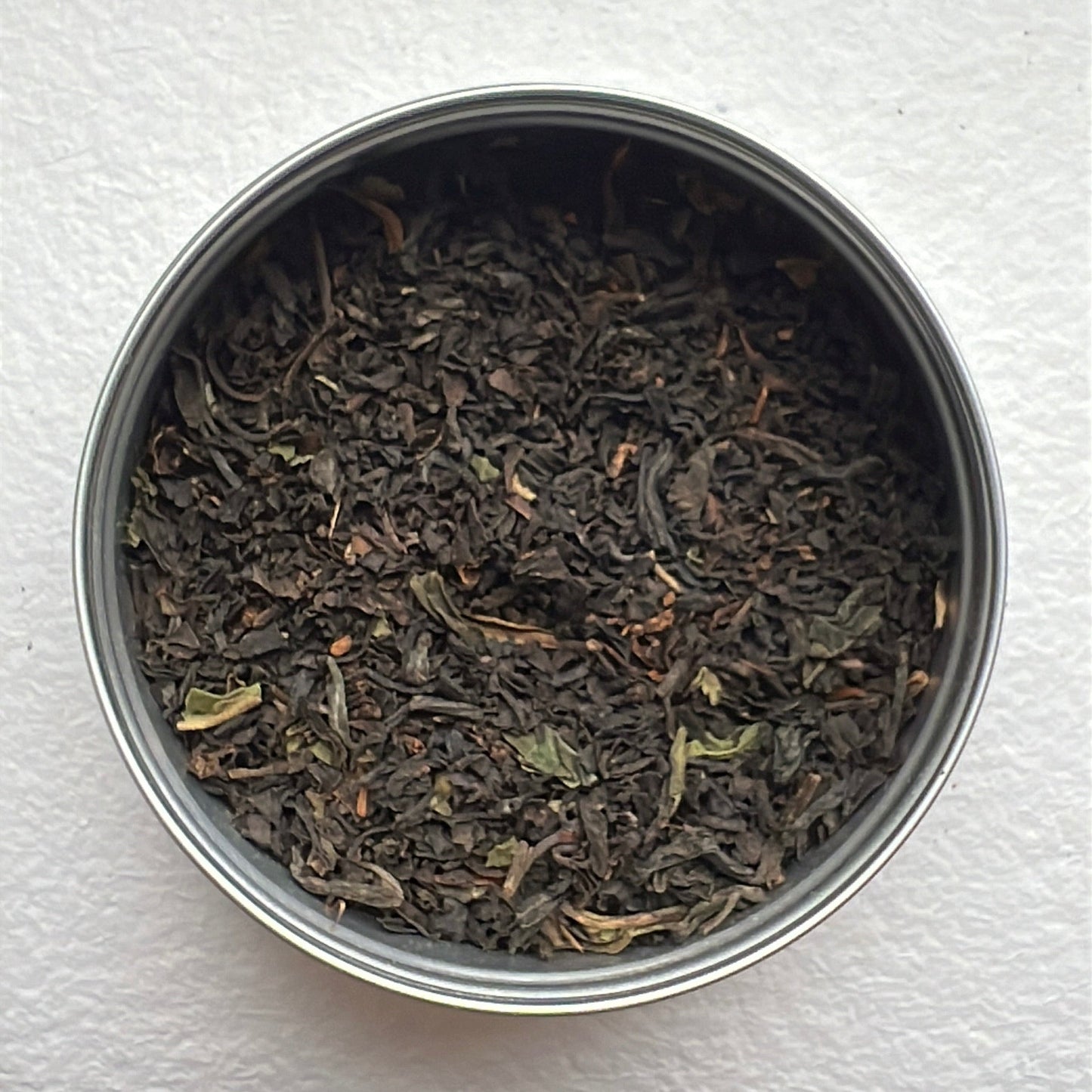 Metal canister filled with black organic tea leaves on a white background by Mull Tea Company