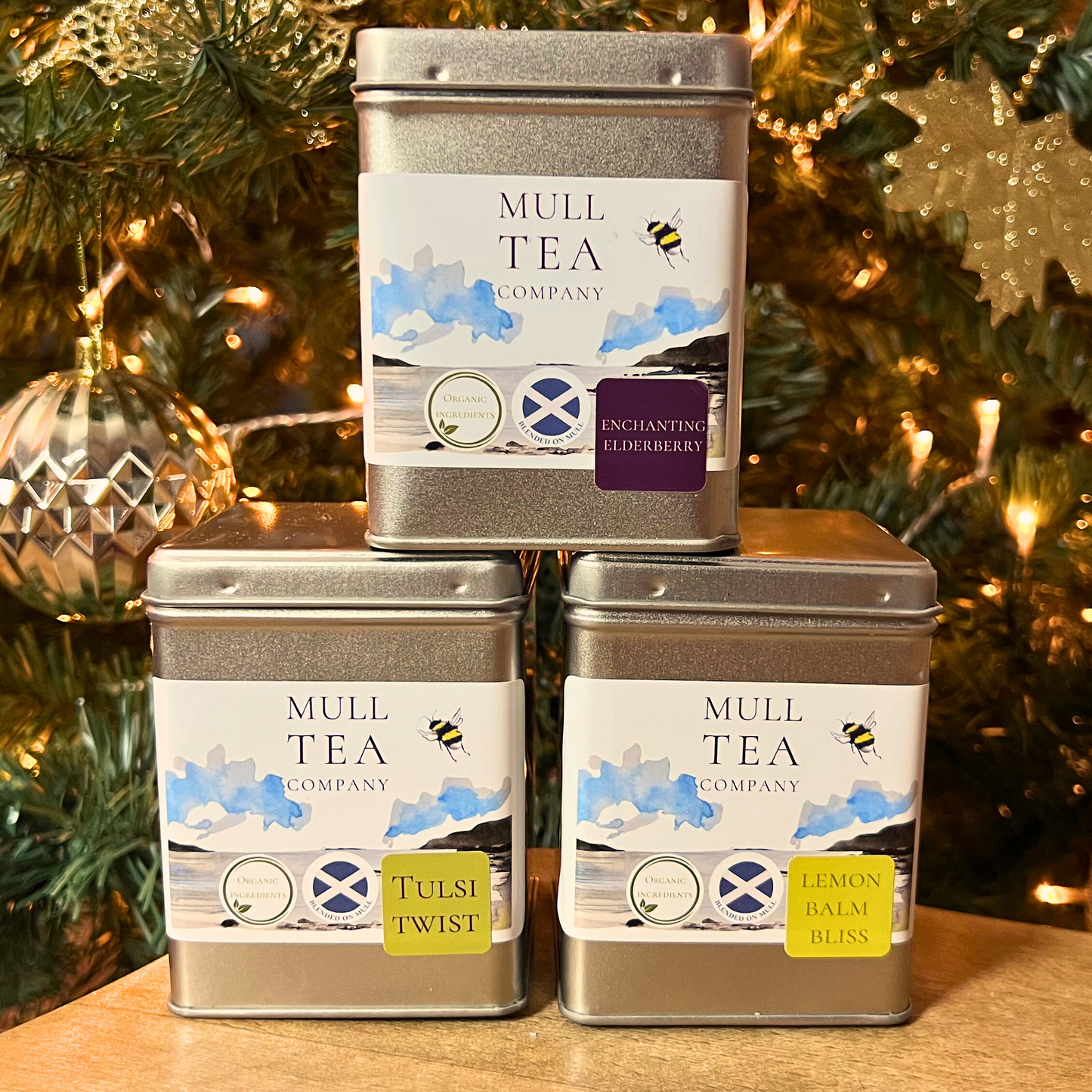 Three organic tea caddies stacked in a triangle in front of a Christmas tree